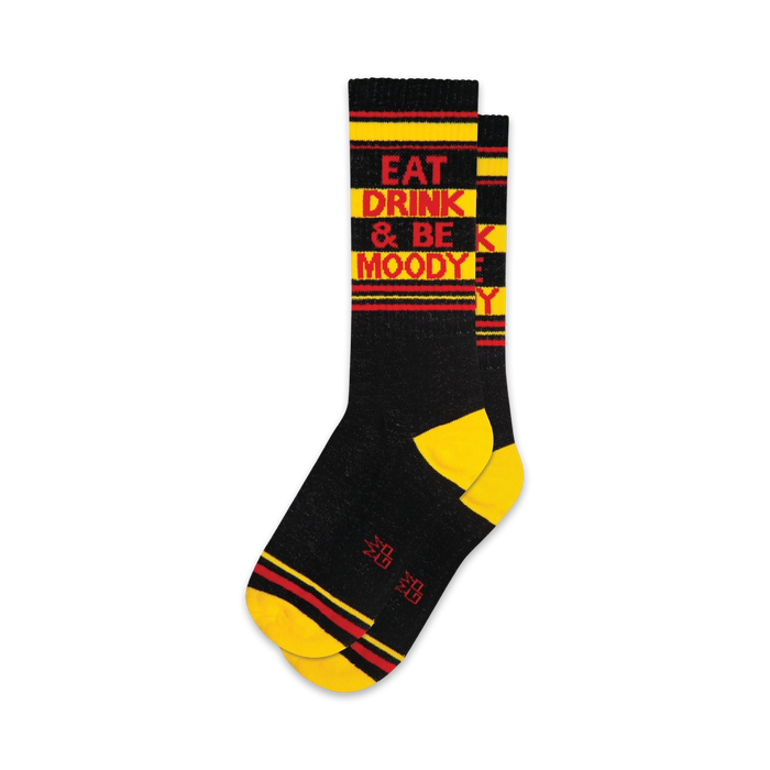 A pair of black crew socks with yellow and red stripes. The socks feature the text 'Eat Drink & Be Moody' in red. }}