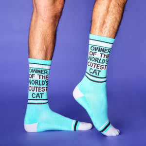 Lifestyle shot of a person modeling the 'Owner of the World's Cutest Cat' socks on their legs against a purple background.