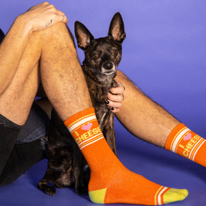 Lifestyle photo of a person wearing the 'I Love Cheese' socks with their dog on a purple background.