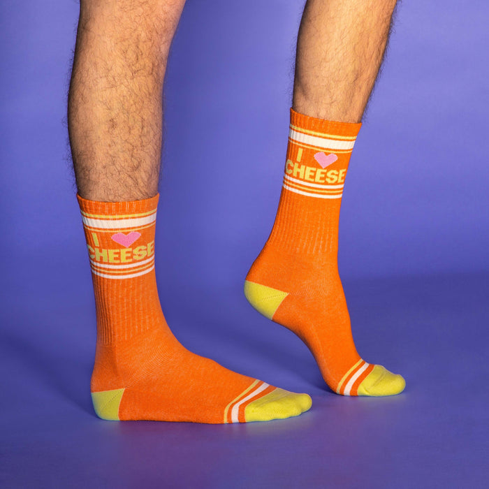 Studio shot of a person's legs modeling the orange 'I Love Cheese' socks against a purple backdrop.