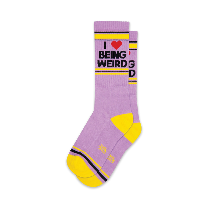 Pair of lavender crew socks with a yellow cuff and heel. The socks feature a graphic that reads 'I love being weird' in black text with a red heart.