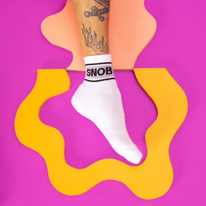 Lifestyle shot of a person's foot wearing a white Snob sock against a colorful background.