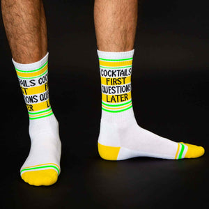 Lifestyle shot: A man's legs wearing the 'Cocktails First Questions Later' socks against a black background.