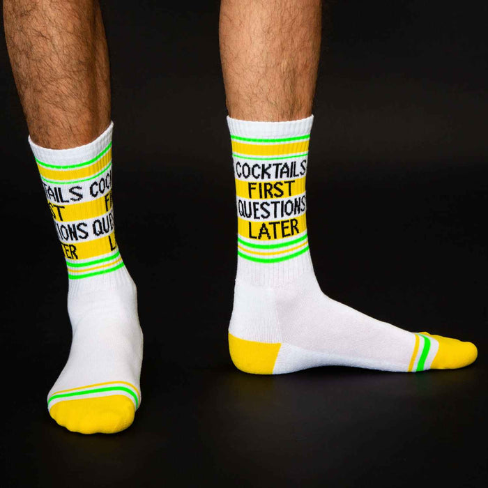Lifestyle shot: A man's legs wearing the 'Cocktails First Questions Later' socks against a black background.
