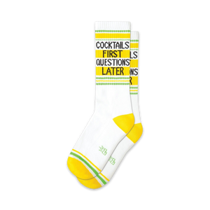 Pair of white crew socks with yellow and lime green stripes.  Text reads: 'Cocktails First Questions Later'.