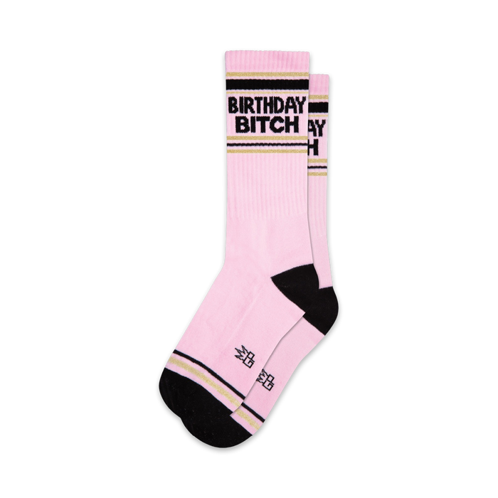 Two pink crew socks with black 'Birthday Bitch' lettering and gold stripes. Black and gold accents at the cuffs. }}