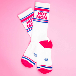 Flat lay of a pair of 'Hot Mom' socks on a pink background.