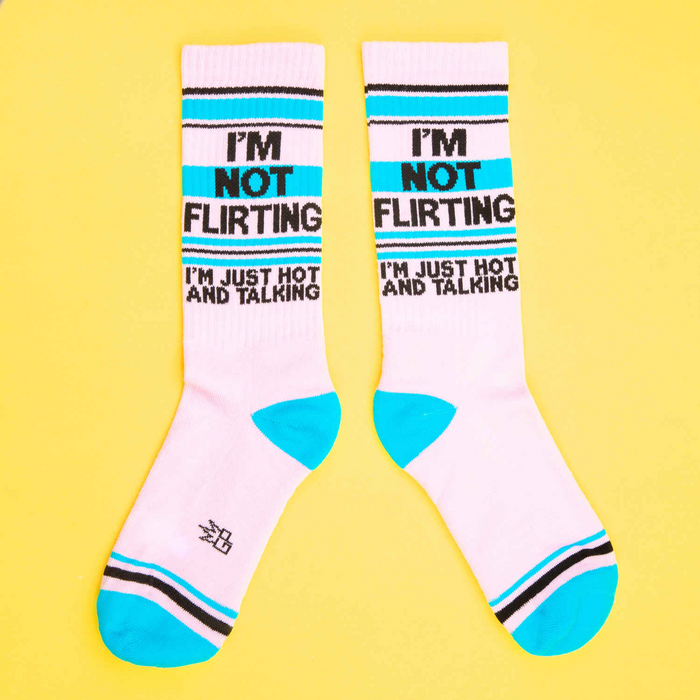 Two 'I'm Not Flirting' socks laid flat, showing the full design. They are pink, teal and black.