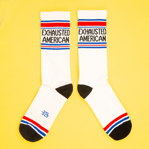 Flat lay product shot of two 'Exhausted American' socks on a yellow background.