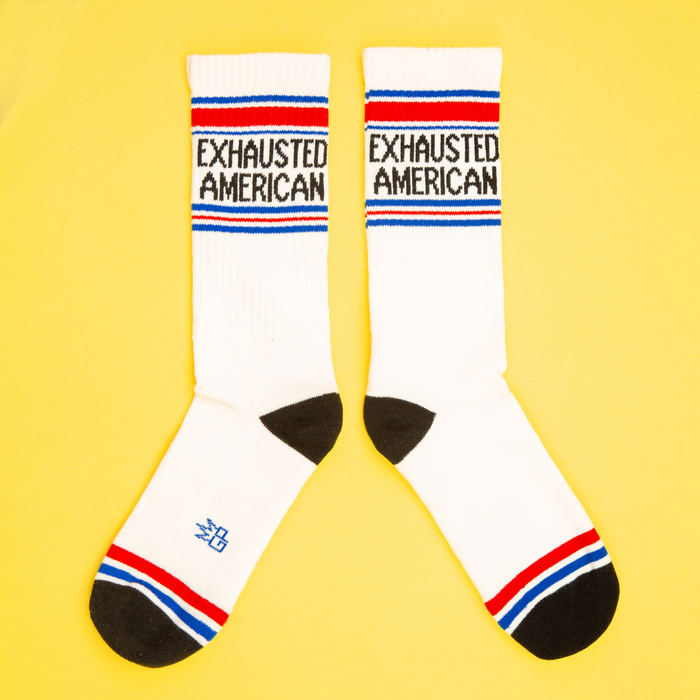 Flat lay product shot of two 'Exhausted American' socks on a yellow background.