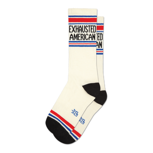 Pair of cream crew socks with 'Exhausted American' text in black, accented by red and blue stripes at the top and bottom.