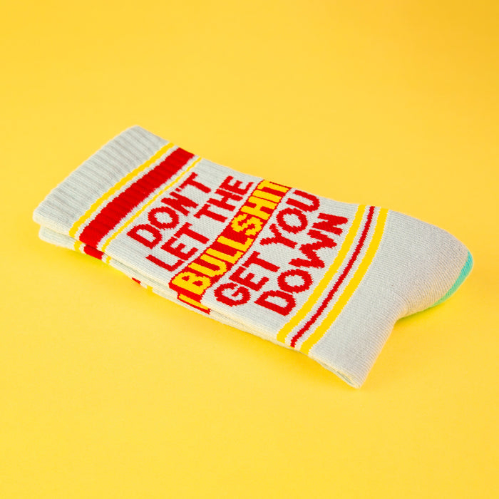 Close-up of a single 'Don't Let The Bullshit Get You Down' sock folded on a yellow background, highlighting the design details.