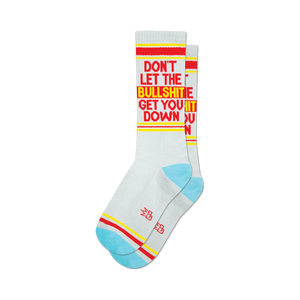 Pair of light grey crew socks with red and yellow text reading 'DON'T LET THE BULLSHIT GET YOU DOWN'.  Features a light blue and red stripe detail at the cuffs.