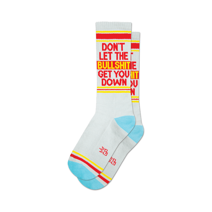 Pair of light grey crew socks with red and yellow text reading 'DON'T LET THE BULLSHIT GET YOU DOWN'.  Features a light blue and red stripe detail at the cuffs.