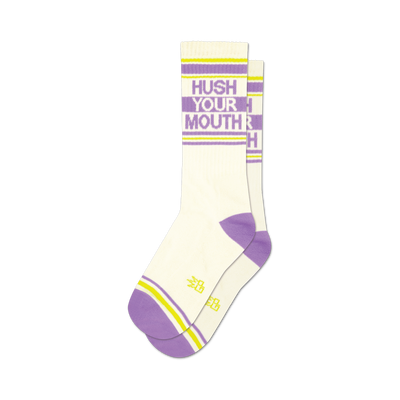 Pair of white crew socks with purple and yellow stripes.  Text 'Hush Your Mouth' is displayed on the socks in purple.