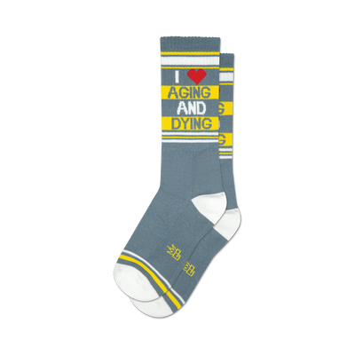 A pair of grey crew socks with yellow stripes and the text 'I ♥ AGING AND DYING' in yellow and red.