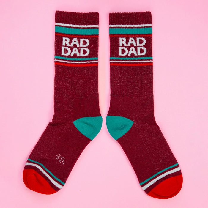 Another flatlay of two maroon Rad Dad socks, this time slightly spread apart, on a pink background.