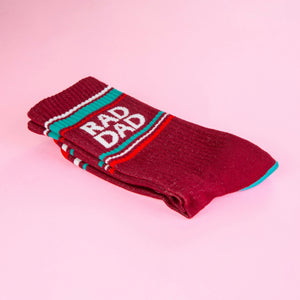 A folded maroon Rad Dad sock on a pink background, showcasing the folded texture and details.