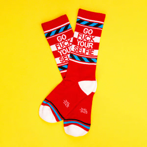 Flat lay of 'Go Fuck Your Selfie' socks on a yellow background. Shows the socks' full design and color.