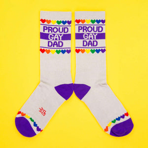 Flatlay of two 'Proud Gay Dad' socks on a yellow background, arranged parallel.
