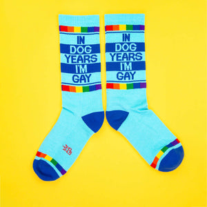 Product shot showcasing 'In Dog Years I'm Gay' socks laid flat and slightly apart on a bright yellow background.