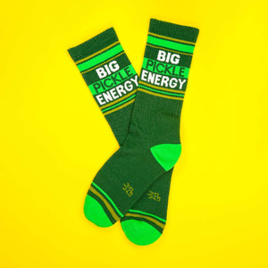 A flat lay of two green 'Big Pickle Energy' socks on a yellow background.