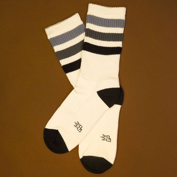 Flat lay product shot of a pair of off-white crew socks with black and grey stripes against a brown background.