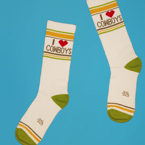 Lifestyle shot of two 'I love cowboys' socks on a blue background, positioned as if they're walking