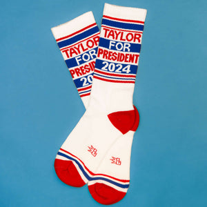 Flat lay of 'Taylor for President 2024' socks on a blue background.