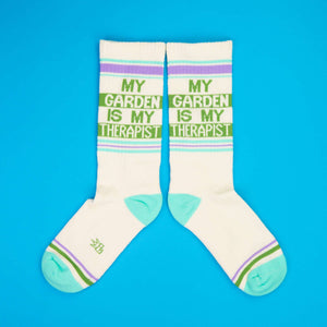 Flat lay product shot showing two 'My Garden Is My Therapist' socks on a bright blue background.