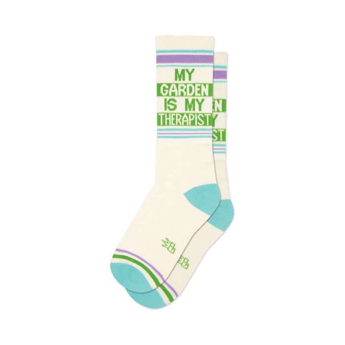 Pair of off-white crew socks with a green 'My Garden Is My Therapist' design and light purple and teal stripes.