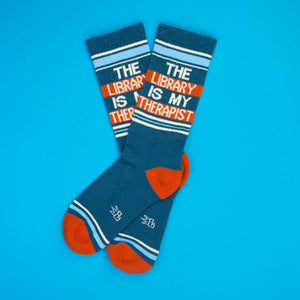 Flat lay of teal 'The Library Is My Therapist' socks on a blue background.