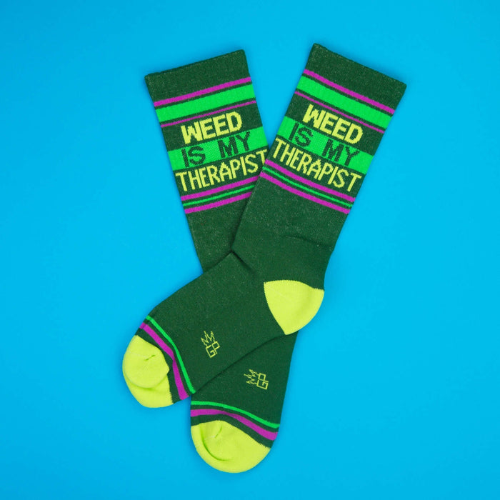 Two 'Weed Is My Therapist' socks lay crossed on a bright blue background.