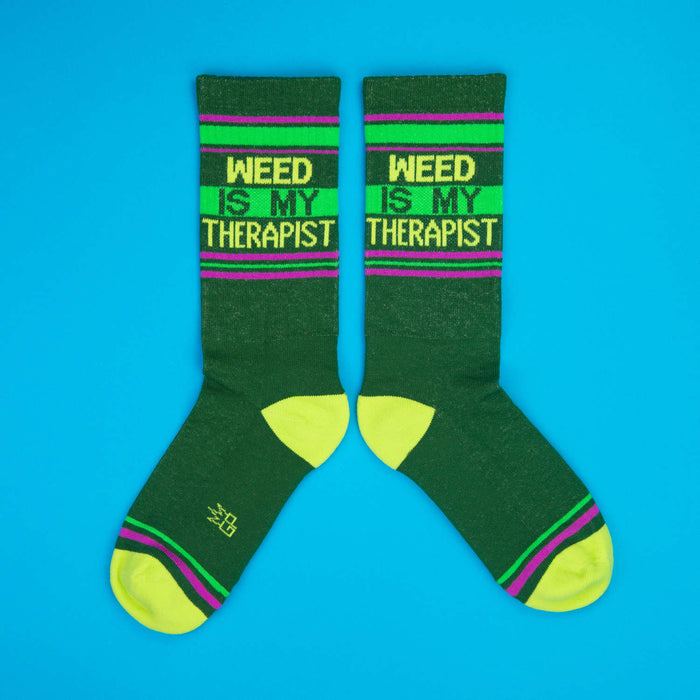 Flatlay product shot showing two 'Weed Is My Therapist' socks on a bright blue background.