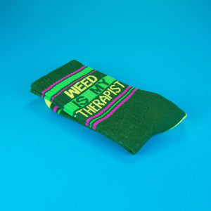 Close-up of a folded 'Weed Is My Therapist' sock on a bright blue background.
