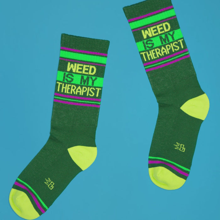 Pair of 'Weed Is My Therapist' socks laid out on a bright blue background.