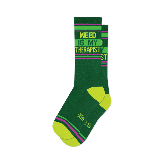 Pair of dark green crew socks with lime green and purple stripes and the text 'Weed Is My Therapist'.