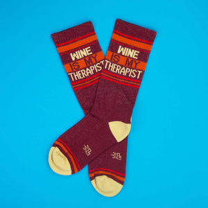 Pair of 'Wine Is My Therapist' socks on a blue background.
