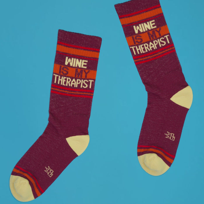 Two 'Wine Is My Therapist' socks laid flat on a blue background.