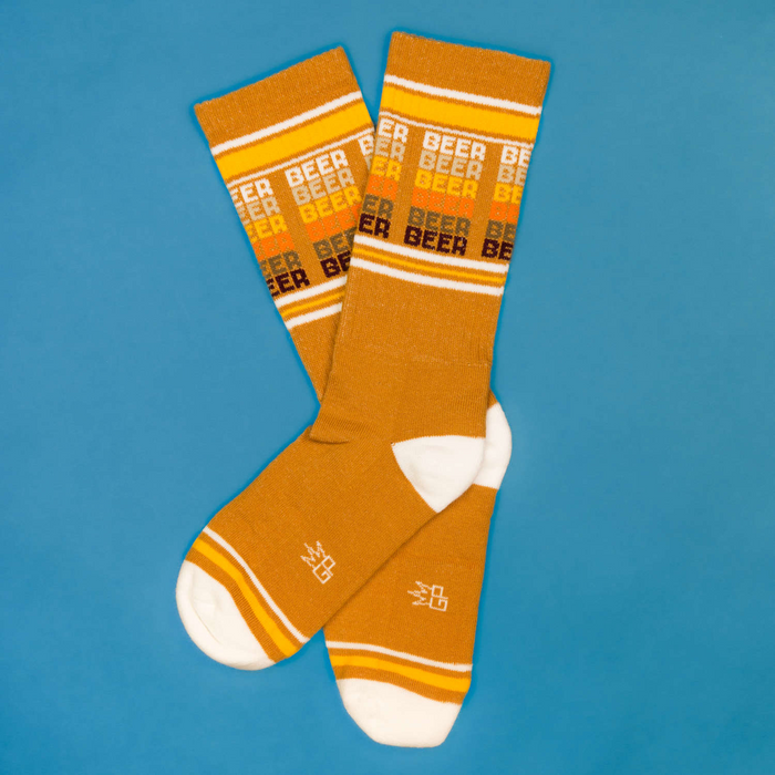 Flatlay product shot of mustard yellow 'Beer' socks on a blue background.