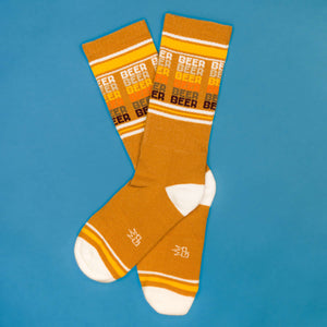 Flatlay product shot of mustard yellow 'Beer' socks on a blue background.