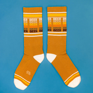 Flatlay product shot of mustard yellow 'Beer' socks on a blue background.