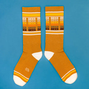 Flatlay product shot of mustard yellow 'Beer' socks on a blue background.