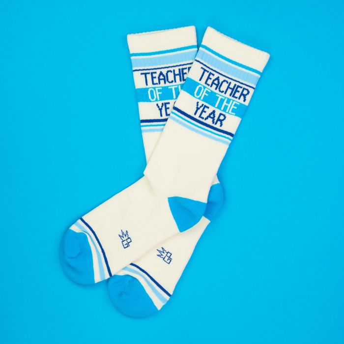 Flatlay of 'Teacher of the Year' socks on a bright blue background.