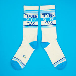 Another flatlay showcasing the 'Teacher of the Year' socks, arranged differently on a blue background.