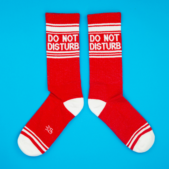 Flat lay of a pair of red 'Do Not Disturb' crew socks on a blue background.