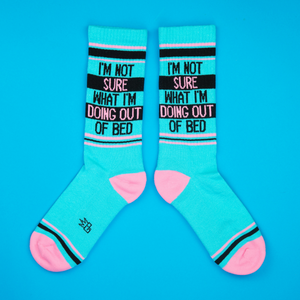 Flat lay of teal 'I'm Not Sure What I'm Doing Out Of Bed' socks against a bright blue background.