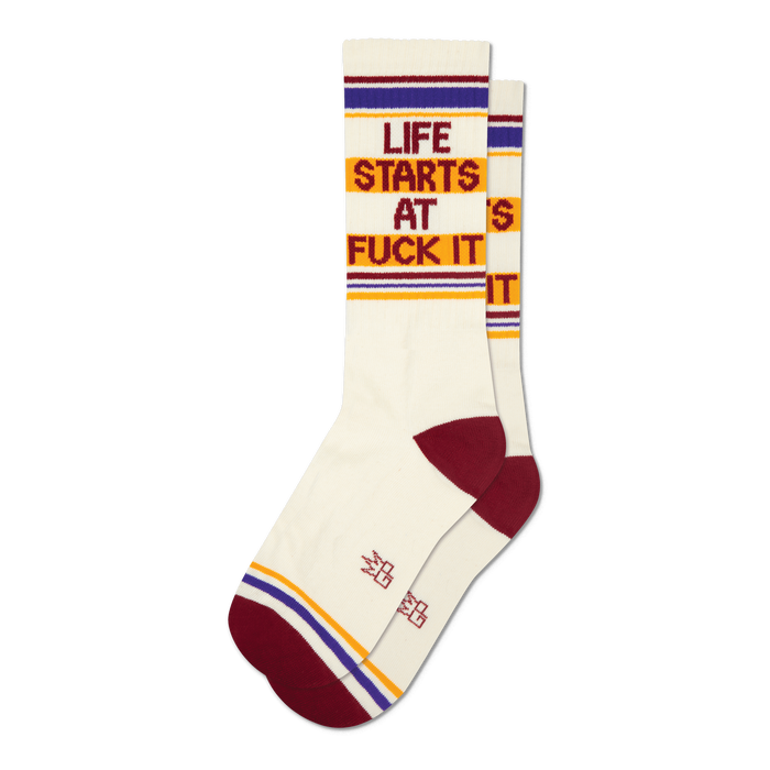 Pair of cream crew socks with maroon, gold, and purple stripes and the phrase 'Life Starts At Fuck It' in a retro font.