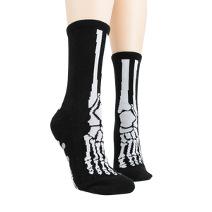 Lifestyle shot of model wearing black skeleton socks with grey non-skid bottoms against a black background.