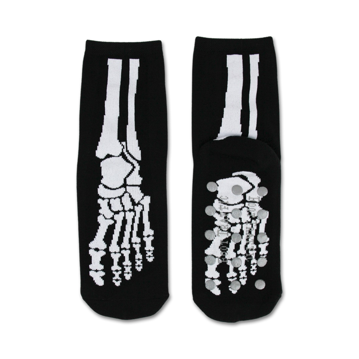 Pair of black non-skid slipper socks with a white skeleton bone design. Grippy dots on the bottom.